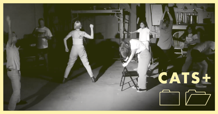 A high contrast black and white video still of 8 performers frozen in various angular poses at different distances from the camera. The performers are wearing everyday clothing, and are in a warehouse with a concrete floor and scaffolding visible in the background. There is a pale yellow frame around the image and a CATS+ logo in the bottom right corner.